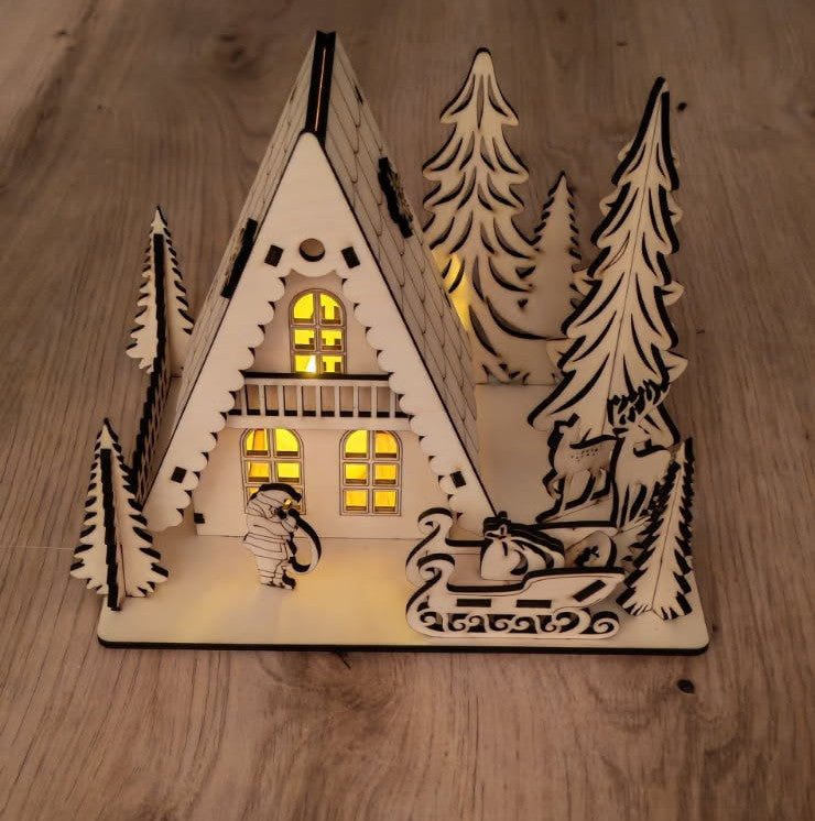 🎄 Un petit village de Noël qui s'illumine ✨
Chalet en bois découpé au laser, entouré de sapins, rennes et traîneau, avec une douce lumière chaleureuse.