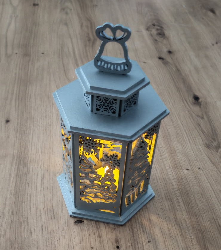 Lanterne de Noël décorative aux motifs hivernaux finement découpés, illuminée par une bougie chauffe-plat LED pour créer une ambiance chaleureuse et féerique.