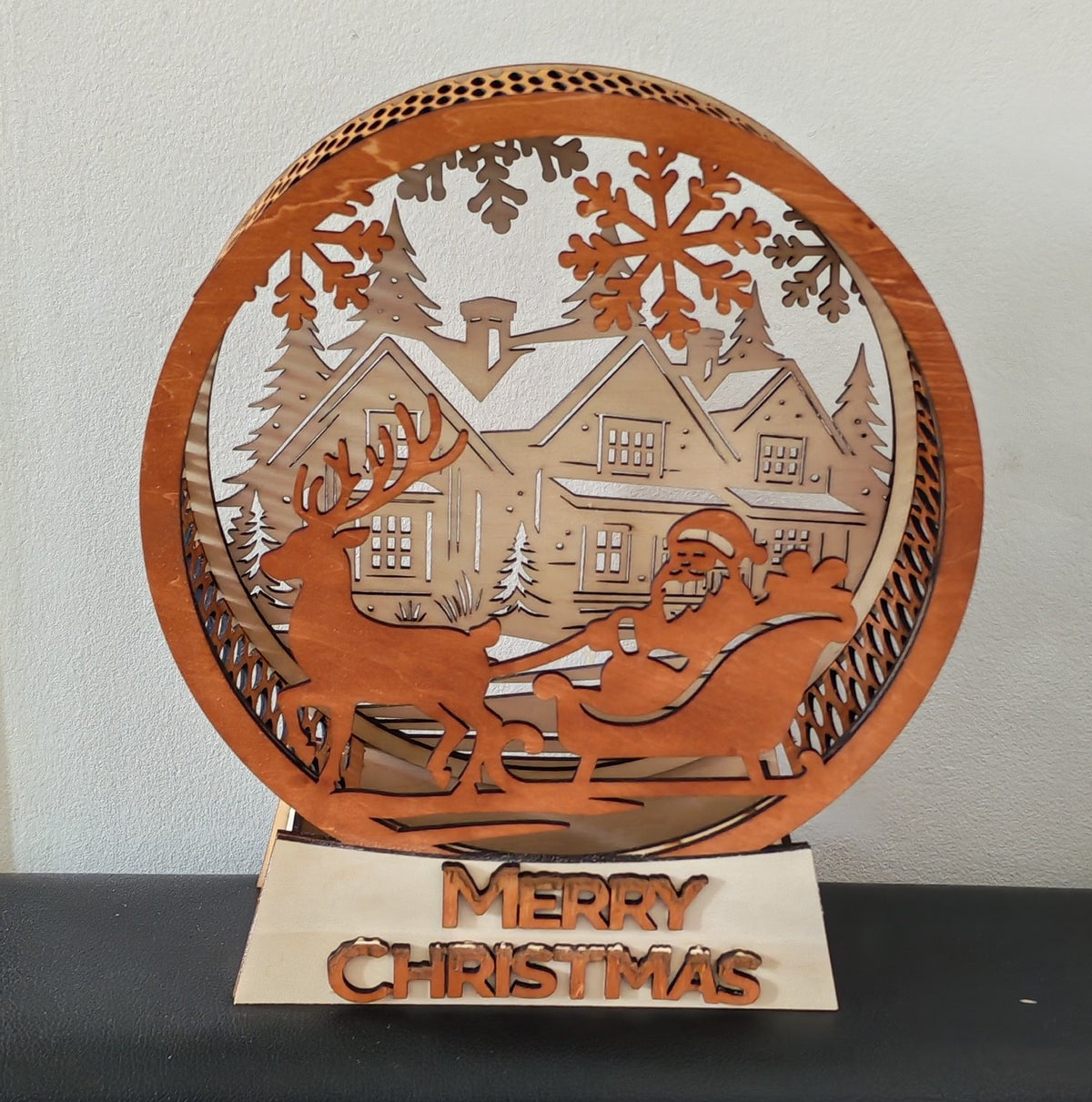 🎅✨ La magie de Noël s'illumine !
Une décoration en bois multicouche représentant le Père Noël et son traîneau devant un village enneigé, sublimée par une douce lumière chaleureuse.