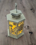 Une lanterne de Noël au charme traditionnel, ornée de décors hivernaux ajourés et illuminée par une bougie chauffe-plat LED pour une ambiance douce et chaleureuse.