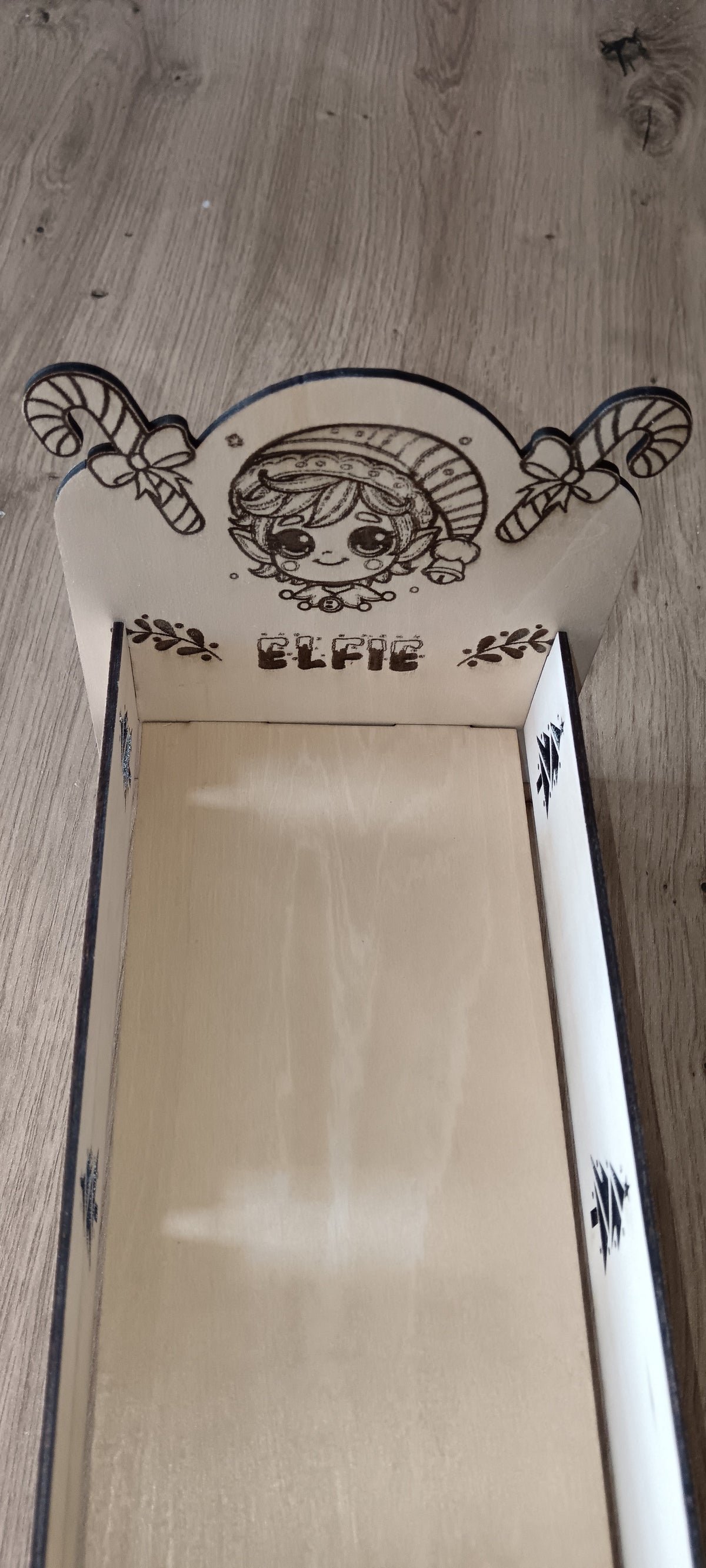 Un petit lit en bois spécialement conçu pour accueillir le lutin farceur pendant la période de Noël, avec prénom personnalisé et décorations gravées.