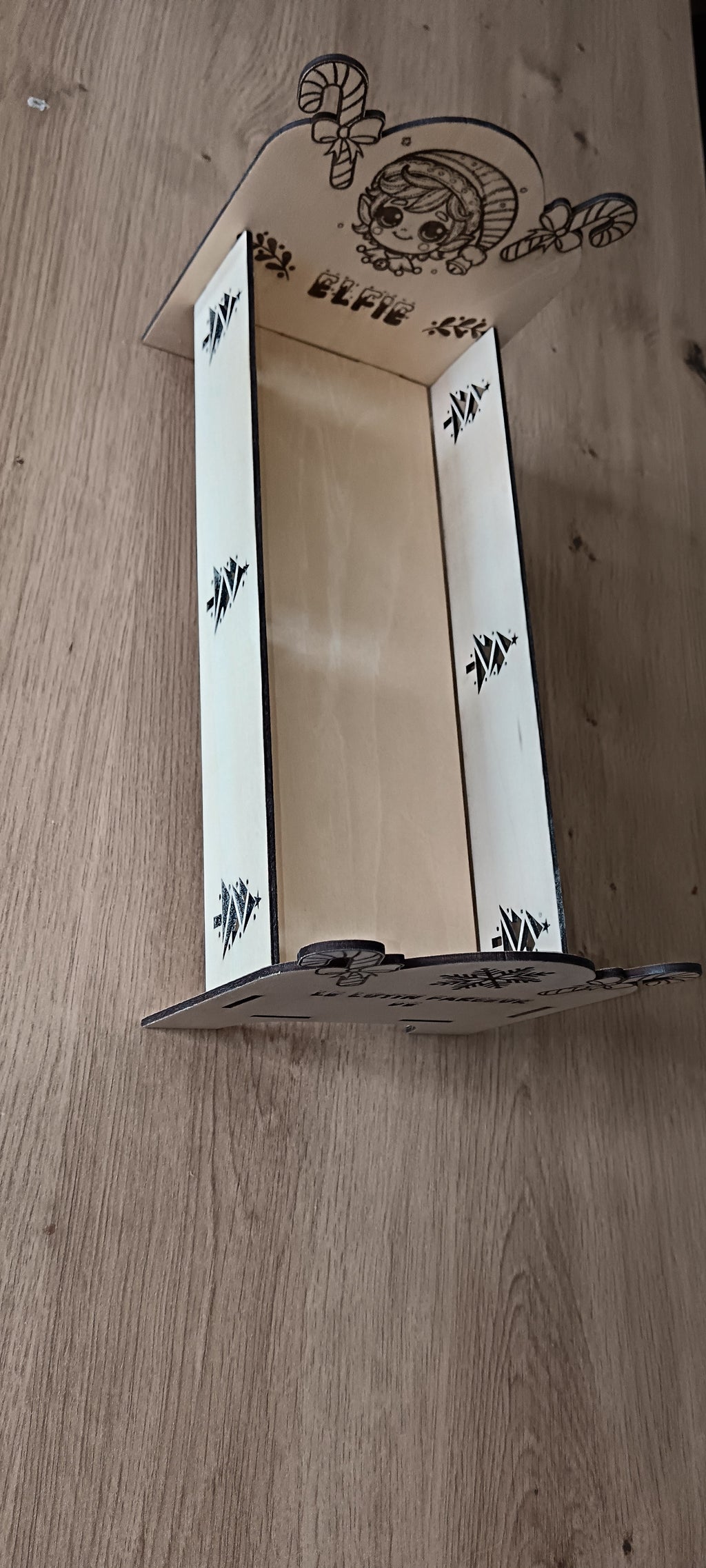 Un petit lit en bois spécialement conçu pour accueillir le lutin farceur pendant la période de Noël, avec prénom personnalisé et décorations gravées.