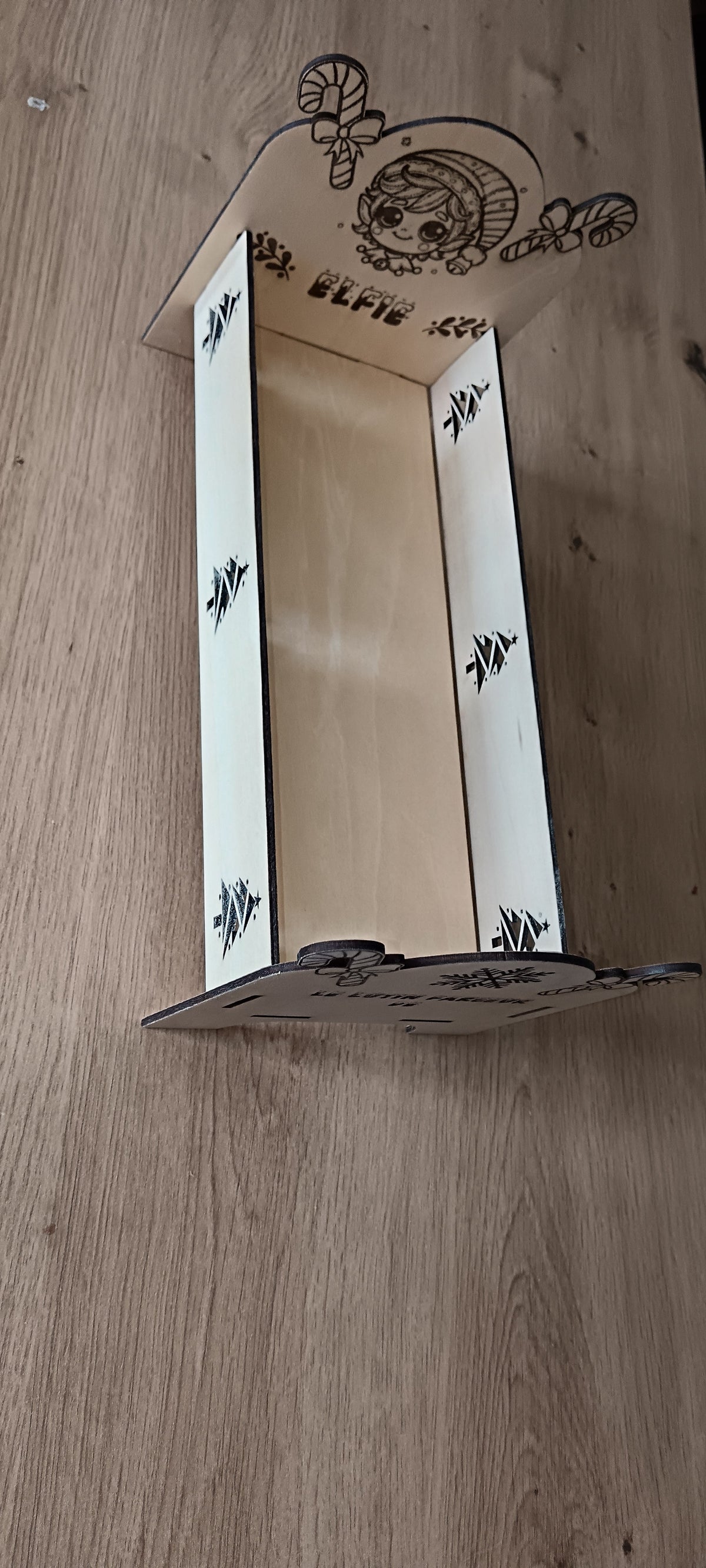 Un petit lit en bois spécialement conçu pour accueillir le lutin farceur pendant la période de Noël, avec prénom personnalisé et décorations gravées.