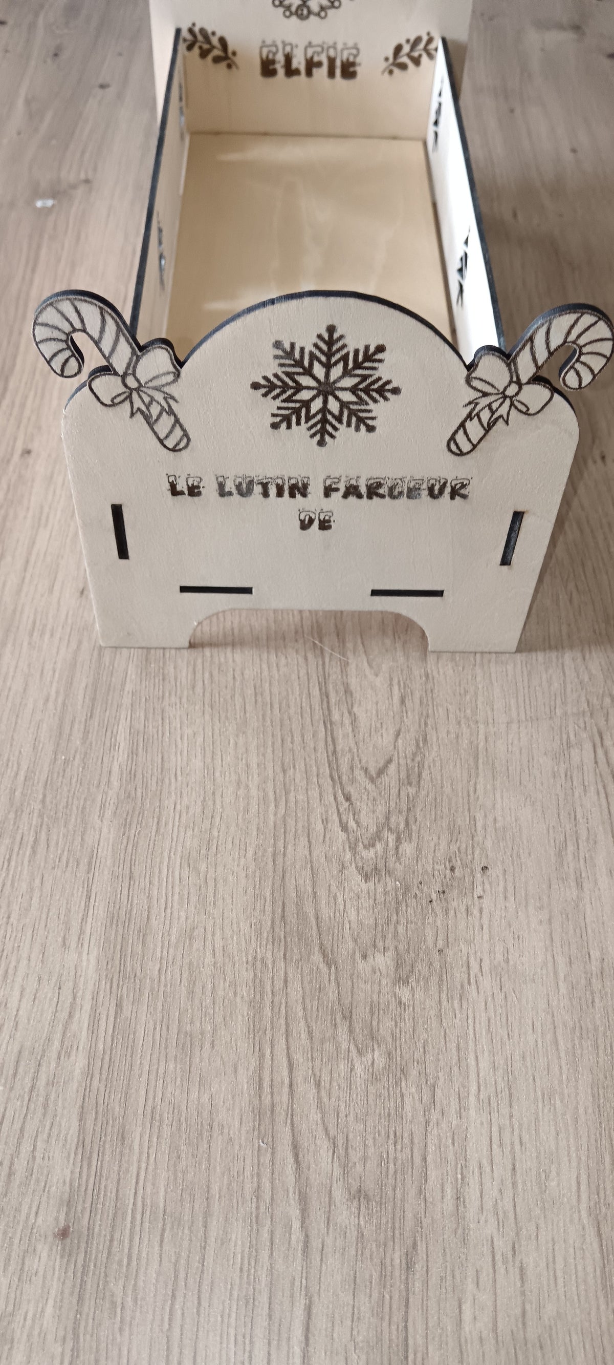 Un petit lit en bois spécialement conçu pour accueillir le lutin farceur pendant la période de Noël, avec prénom personnalisé et décorations gravées.