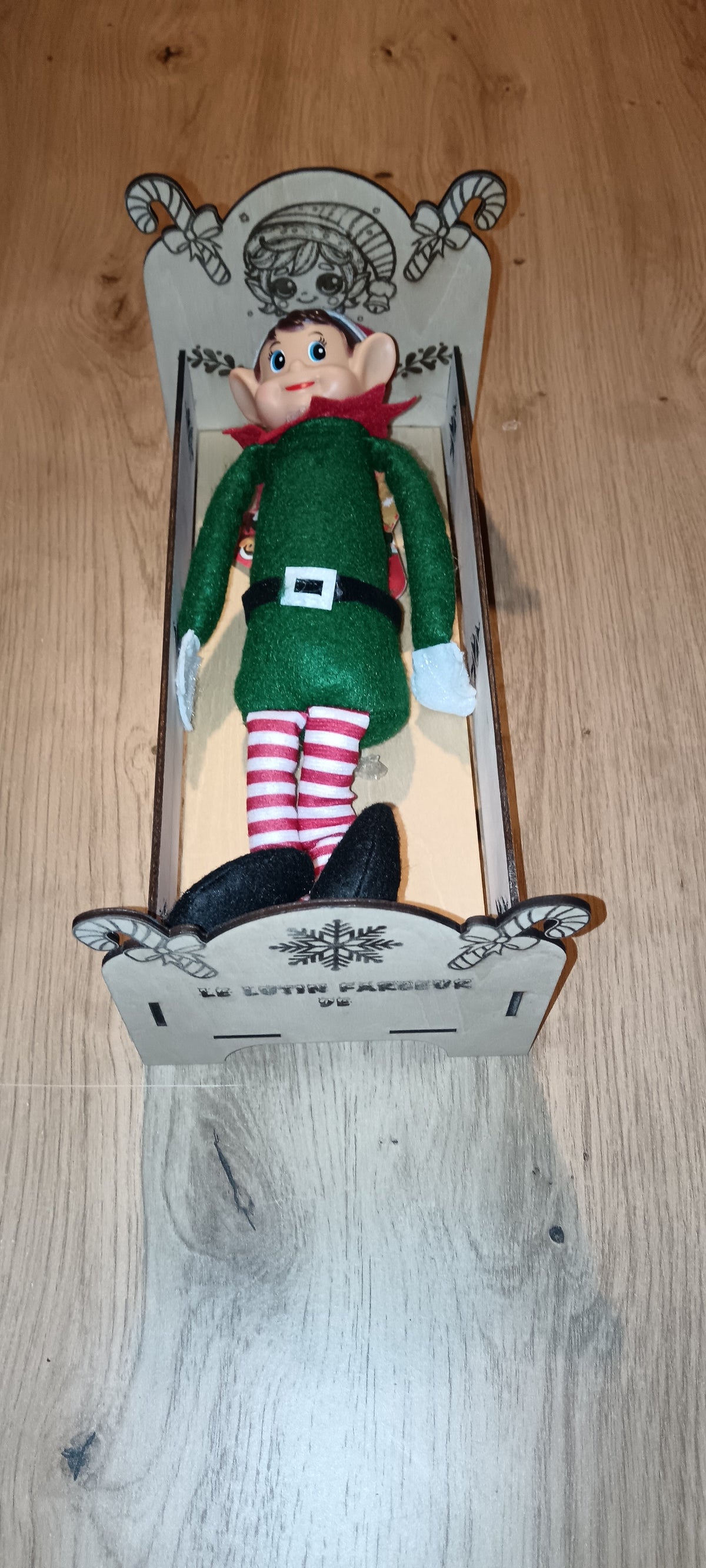 Un petit lit en bois spécialement conçu pour accueillir le lutin farceur pendant la période de Noël, avec prénom personnalisé et décorations gravées.