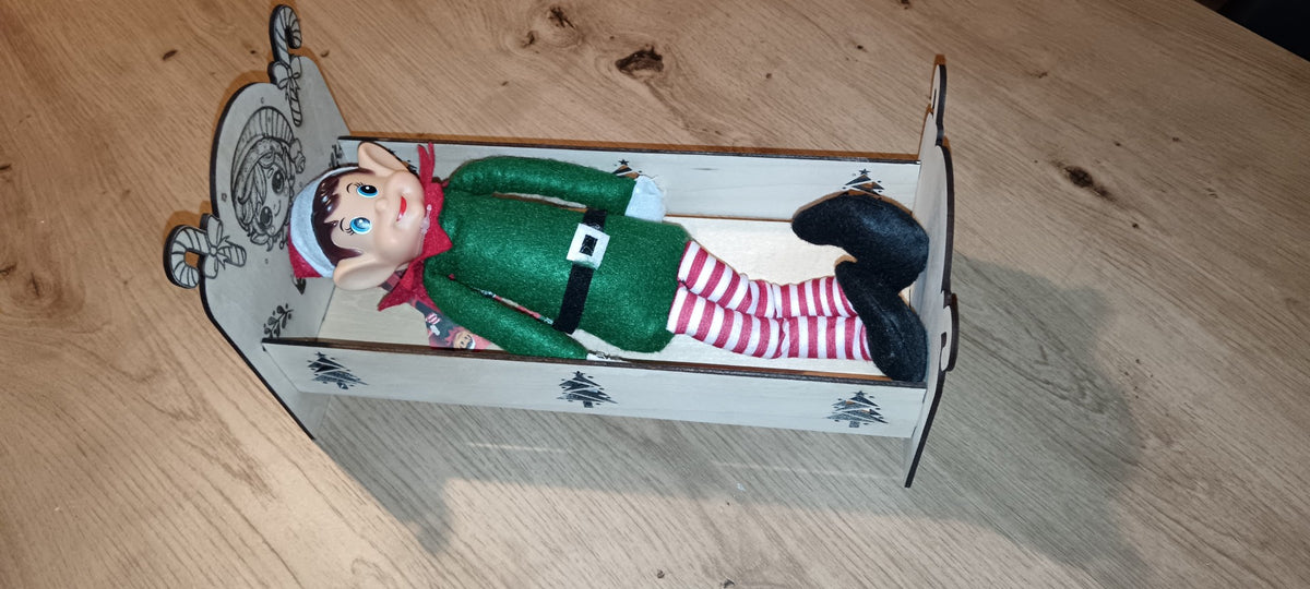 Un petit lit en bois spécialement conçu pour accueillir le lutin farceur pendant la période de Noël, avec prénom personnalisé et décorations gravées.