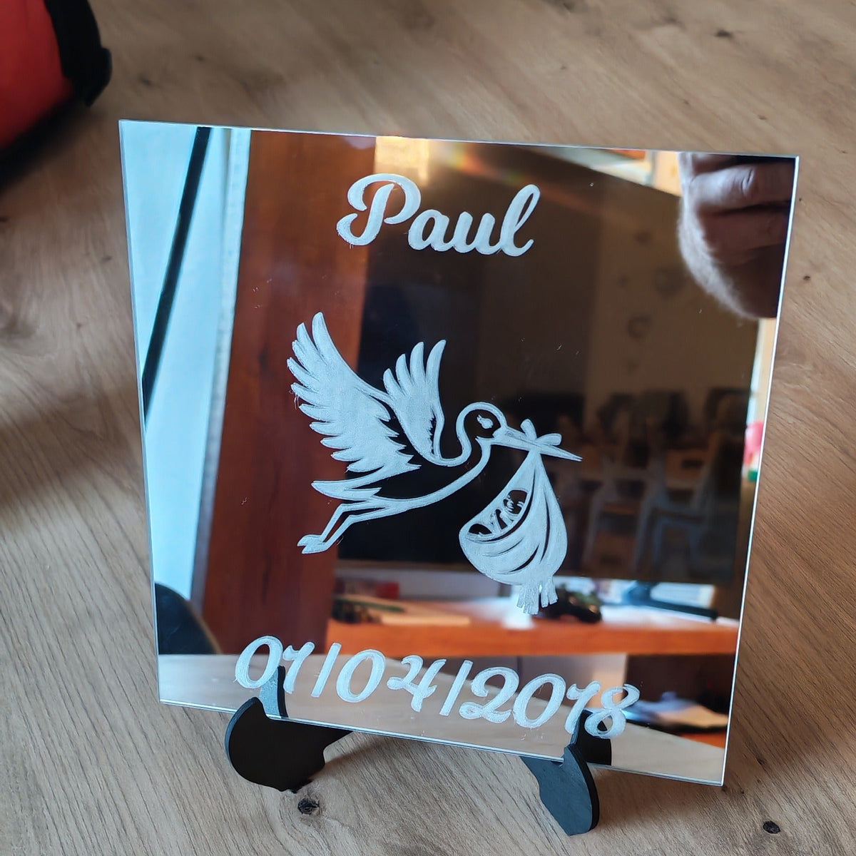 Miroir de naissance posé sur un chevalet noir, gravé du prénom Paul, d’une date de naissance et d’une cigogne portant un bébé.