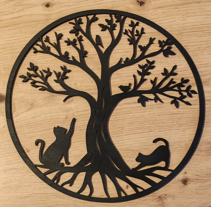 Arbre de vie circulaire en bois noir ajouré, avec deux chats au pied du tronc, posé sur une surface en bois clair