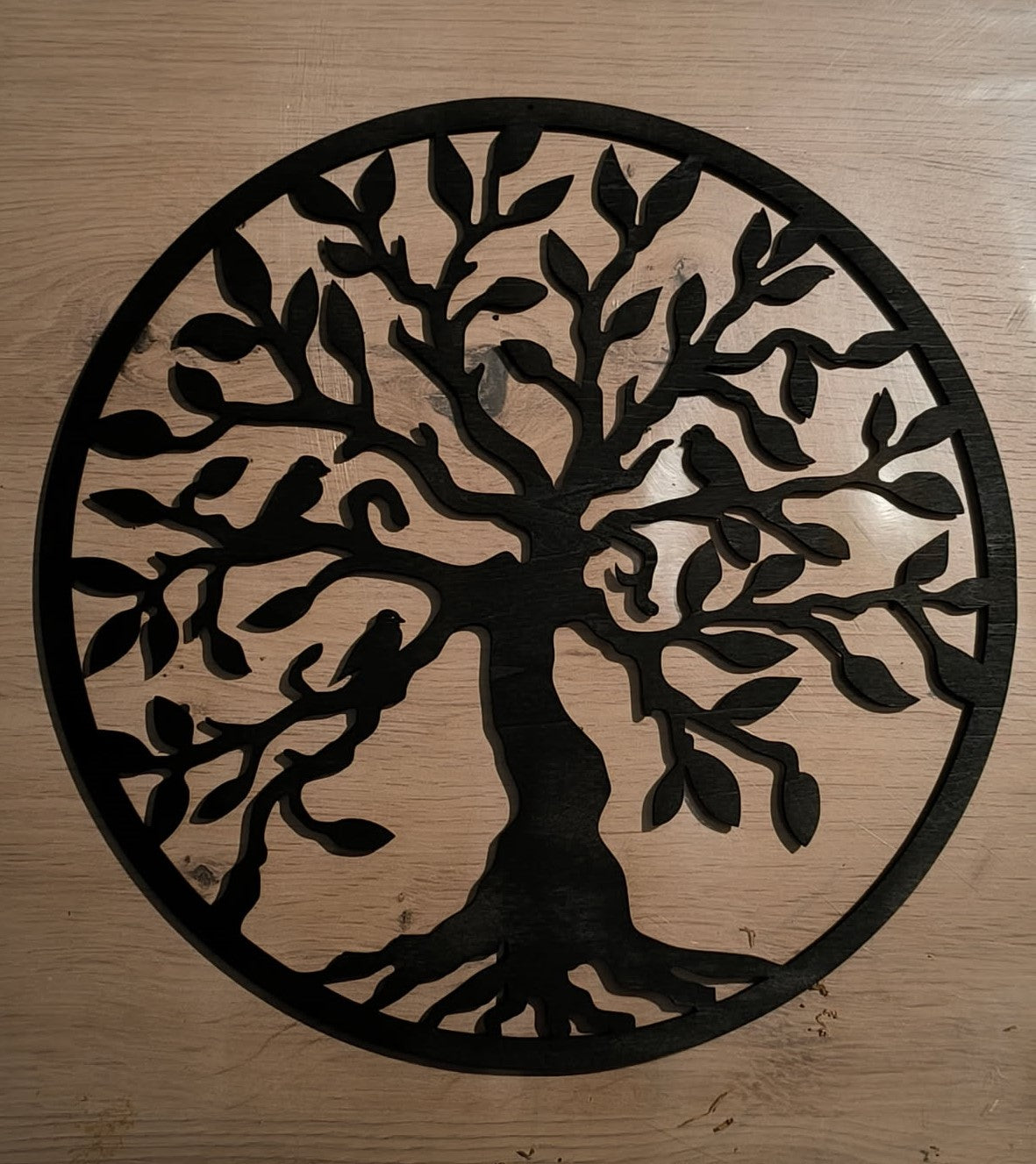 Arbre de vie mural en bois noir ajouré, avec branches et racines dans un cadre circulaire, sur un fond en bois