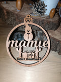 Boule de Noël en bois ajouré avec inscription Mamie, bonhomme de neige et cadeaux, posée devant des rondins