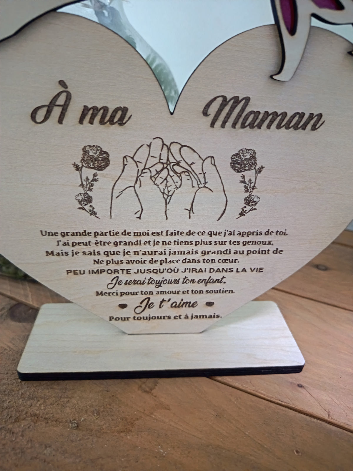 Détail du cœur en bois gravé À ma Maman, avec dessin de mains, roses et message affectueux, posé sur son socle