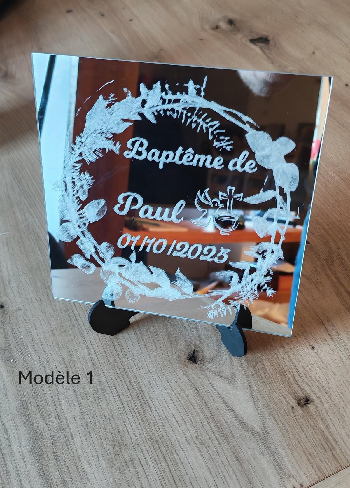 Miroir de baptême sur chevalet noir, gravé du prénom Paul, de la date du baptême et d’une couronne végétale avec des symboles de cérémonie.
