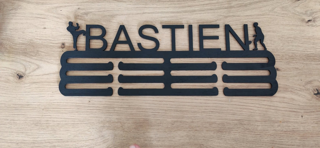 Support de médailles en bois noir personnalisé au prénom Bastien, avec silhouettes sportives